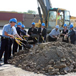 people in hardhats shoveling dirt in front of a backhoe